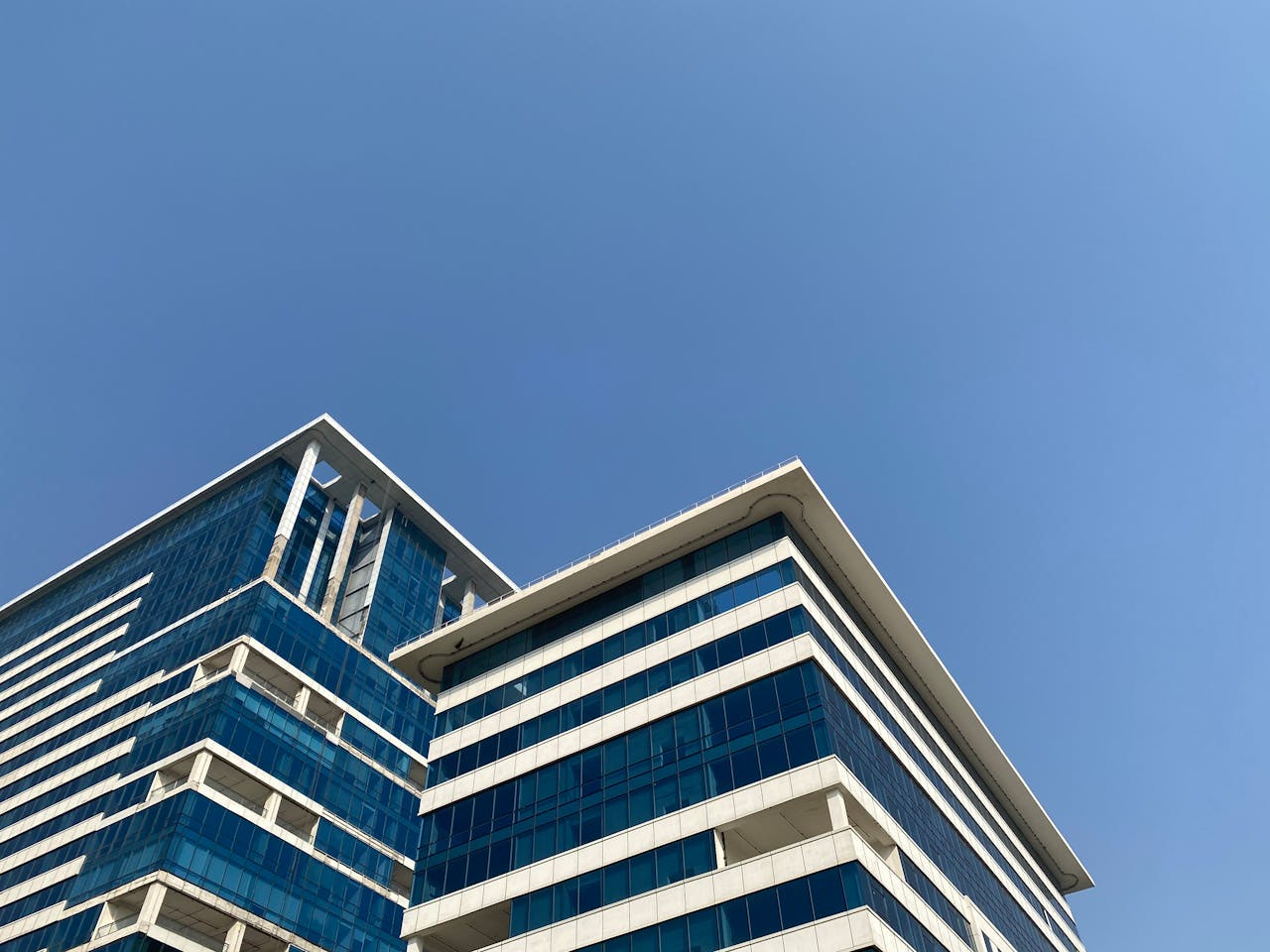 Low angle shot of a modern office building against a clear blue sky in Gurugram, India.